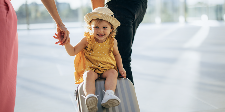 Une petite fille est assise sur une valise tirée en avant, capturant un moment ludique de voyage en famille et illustrant les conseils Photobox pour voyager avec des enfants.