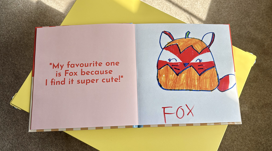 Un album photo enfant ouvert présente à gauche une légende et une citation d'une petite fille expliquant son œuvre, accompagnée de son dessin correspondant d'un renard de dessin animé à droite, illustrant les conseils de Photobox pour ajouter du texte à un album photo enfant.