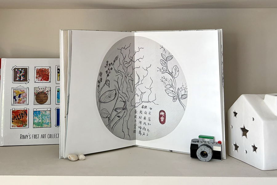 Un album photo enfant ouvert présente une double page de croquis d'arbres accompagnés de texte, à côté d'un album fermé dont la couverture façon scrapbook réunit divers exemples de dessins d'enfants, illustrant le souvenir précieux que crée un album photo enfant Photobox.