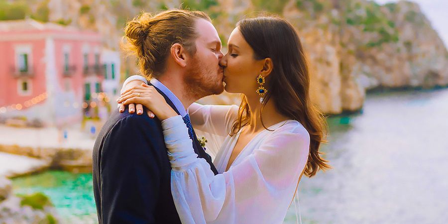 Une mariée et un marié s’embrassent le jour de leur mariage devant un décor d’inspiration méditerranéenne, illustrant la romance des tendances mariage 2026 et du style de mariage personnalisé Photobox.