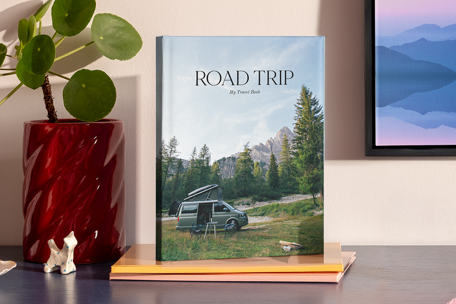 Un grand livre photo au format portrait présente une photo d'un camping-car dans un paysage montagneux digne d'un parc national, illustrant les idées de titre album photo road trip de Photobox.