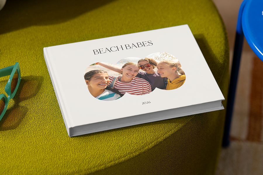 Un livre photo avec quatre filles souriantes sur la couverture s'intitule 'Beach Babes', illustrant les idées de titre album photo voyage entre amis de Photobox.