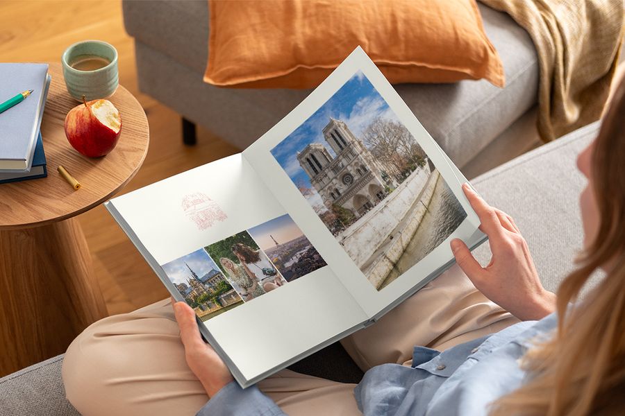Une femme tient sur ses genoux un livre photo ouvert montrant différentes photos de voyage, illustrant le design Graphic Getaways de Photobox inspiré des affiches de voyage vintage et des cartes de villes illustrées.