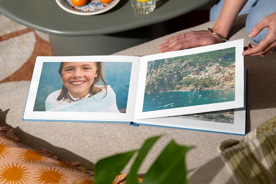 Un livre photo ouvert présente une jeune fille souriante au bord de la mer sur une page et une vue de plage sur l'autre, illustrant le design Holiday Escape de Photobox avec une photographie immersive pleine page.