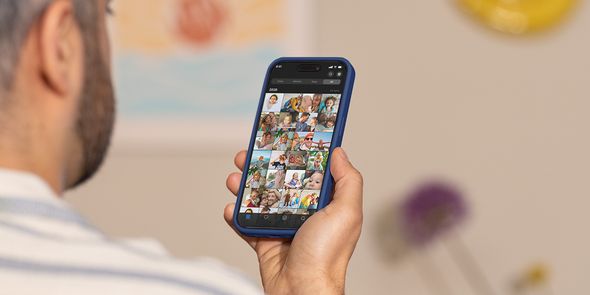 Un homme tient son téléphone et fait défiler sa pellicule photo, illustrant le guide de Photobox pour gérer la surcharge de photos et trier ses clichés.