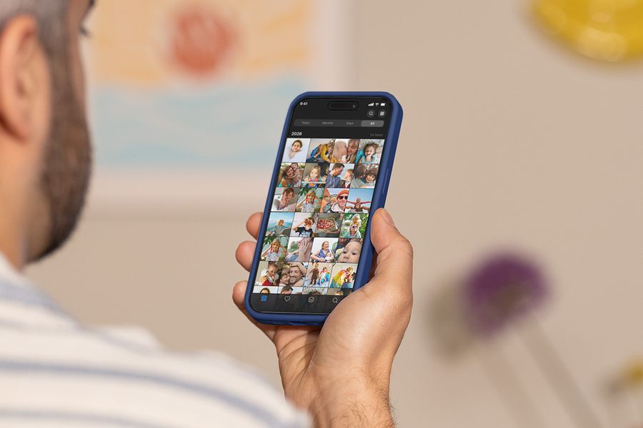 Un homme tient son téléphone et fait défiler sa pellicule photo, illustrant le guide de Photobox sur les meilleurs outils pour organiser ses photos.