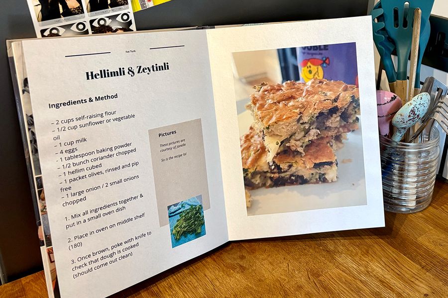 Un livre photo recette ouvert est posé dans une cuisine, avec un pot de cuillères et d'ustensiles de cuisine en arrière-plan, illustrant les conseils de Photobox pour choisir les recettes à inclure avant de créer son propre livre de recettes.