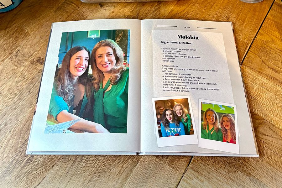 Une double page du livre photo recette personnalisé de Sarah présente une recette de molohia, accompagnée de photos de famille plutôt que d'une image du plat, illustrant le conseil de Photobox d'inclure des photos personnelles pour rendre un livre de recettes vraiment significatif.