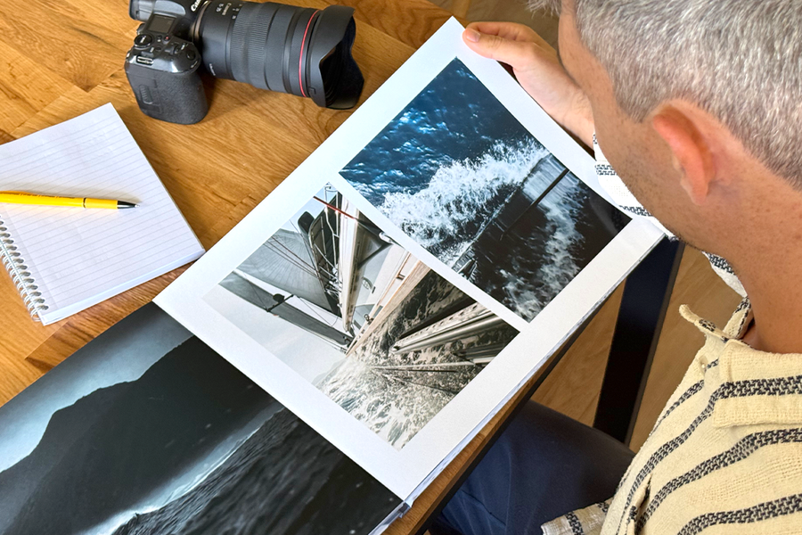 Le photographe Charl van Rooy regarde son portfolio, avec son appareil photo et un carnet posés sur la table à côté de lui, illustrant les conseils de Photobox pour choisir les meilleurs modèles et mises en page pour un portfolio photographique.