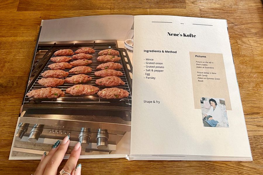 Une double page ouverte du livre de recettes de Sarah présente la recette de kofte de sa Nene, avec la main manucurée d'une femme posée sur le livre, sur un plan de travail en bois, illustrant les conseils de la check-list finale de Photobox avant d'imprimer un livre de recettes personnalisé.