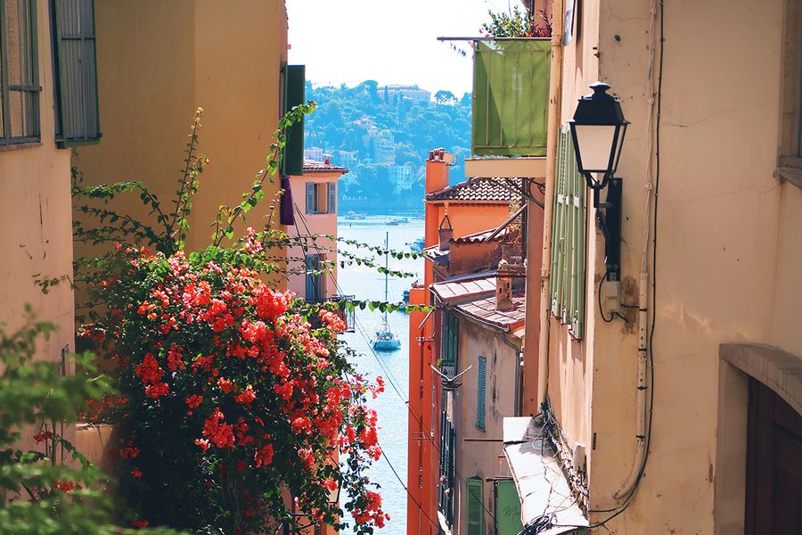 Une rue étroite bordée de fleurs mène vers la mer à Nice, illustrant le charme d'des vacances en septembre dans le sud de la France.