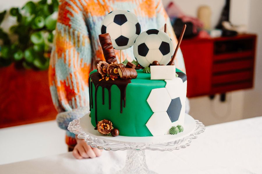 Un gâteau d'anniversaire d'enfant décoré de ballons de foot et de barres chocolatées, illustrant le conseil de Photobox de photographier le gâteau star avant l'arrivée des invités.