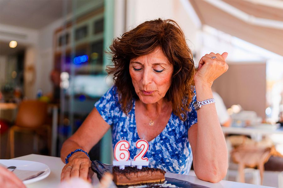 Une femme souffle les bougies indiquant « 62 » sur son gâteau d'anniversaire, illustrant le conseil de Photobox de capturer le moment précis où les bougies s'éteignent.