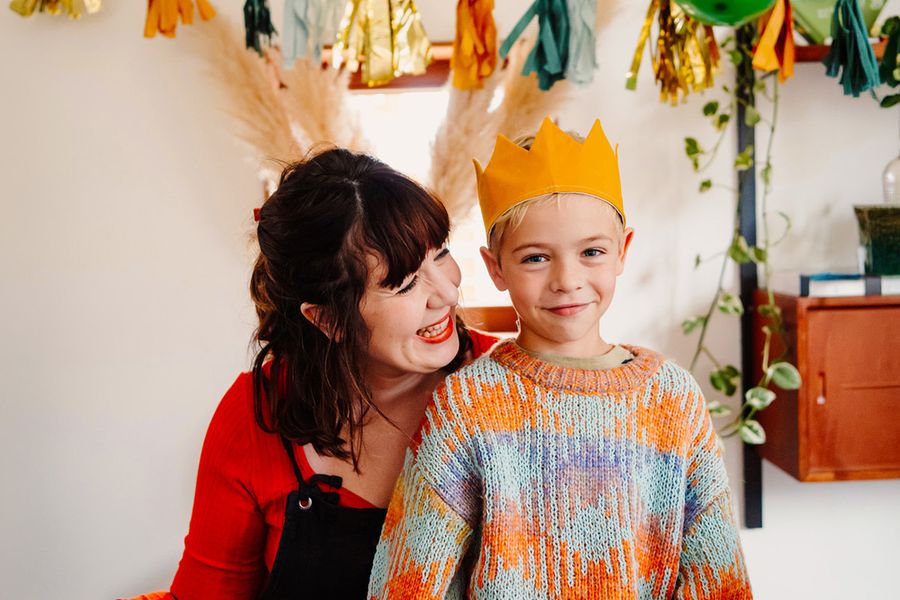 Un jeune garçon souriant porte une couronne d'anniversaire tandis qu'une femme plus âgée le regarde en souriant, illustrant la check-list ultime de Photobox pour la séance photo d'anniversaire.