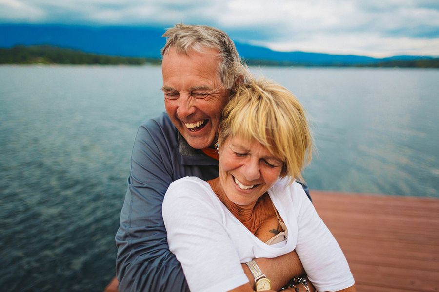 Un couple plus âgé s'enlace et sourit près d'un magnifique lac, illustrant les idées de Photobox pour savoir quoi écrire dans une carte pour un anniversaire de mariage marquant.