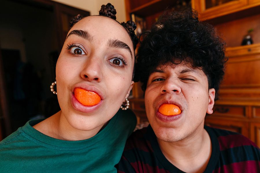 Un couple fait des grimaces avec des tranches d'orange dans la bouche, illustrant les idées de Photobox pour des messages drôles à écrire dans une carte d'anniversaire de mariage.