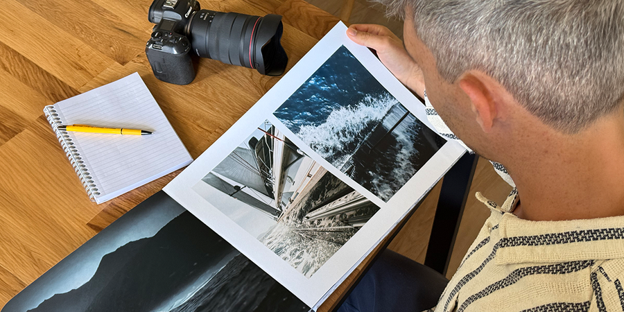 Le photographe Charl van Rooy regarde son portfolio, avec son appareil photo et un carnet posés sur la table à côté de lui, présentant le guide de Photobox pour créer un portfolio photo sous forme de livre.