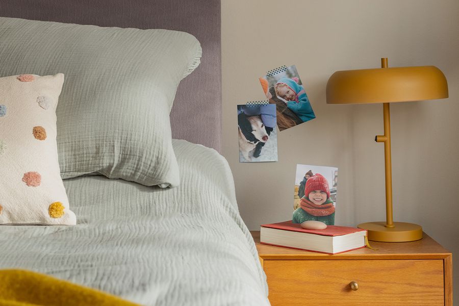Une sélection de tirages photo de famille est accrochée au mur à côté d'un lit, illustrant comment les tirages photo Photobox apportent une touche chaleureuse et personnelle à une chambre hygge.