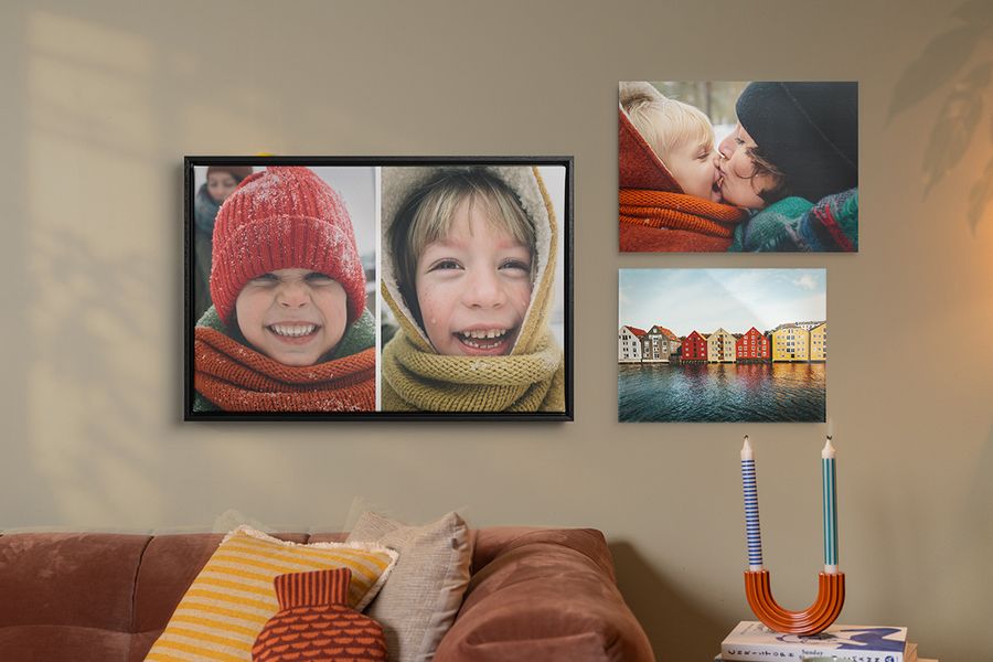 Trois exemples de décoration murale personnalisée sont accrochés au-dessus d'un canapé dans un salon, des tirages de famille aux couleurs d'automne avec des enfants souriants en tenue d'hiver, illustrant comment la décoration murale Photobox apporte un style hygge chaleureux à la maison.
