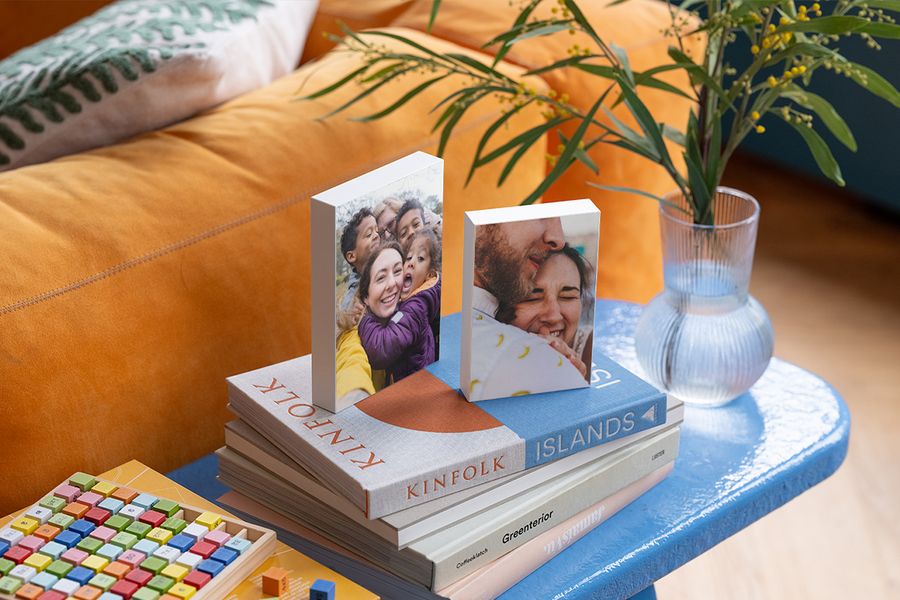 Deux blocs photo personnalisés sont posés sur une sélection de beaux livres sur une table d'appoint bleue à côté d'un canapé en velours orange, illustrant comment les blocs photo Photobox apportent une touche personnelle à une maison hygge.
