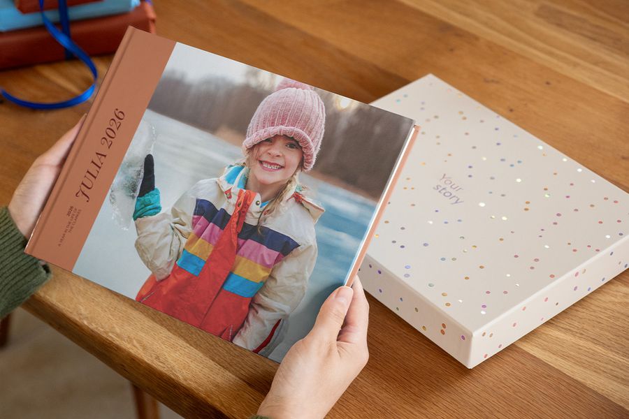 Quelqu'un tient un livre photo intitulé « Julia », avec une petite fille souriante sur la couverture, avec une boîte cadeau de présentation posée sur la table juste derrière, illustrant pourquoi une boîte pour livre photo rend une création encore plus spéciale.