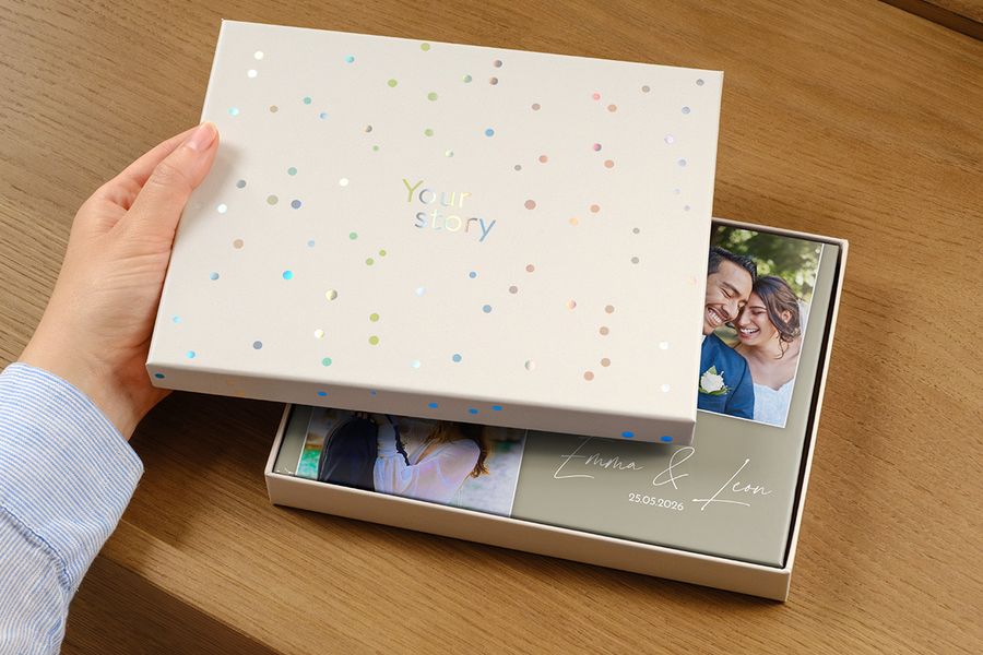Un livre photo de mariage est posé dans la nouvelle boîte de présentation, sa couverture montrant une photo du couple et la date du mariage en guise de titre, partiellement cachée par le couvercle entrouvert de la boîte cadeau, illustrant pourquoi une boîte de présentation est un bon choix pour un album de mariage haut de gamme.
