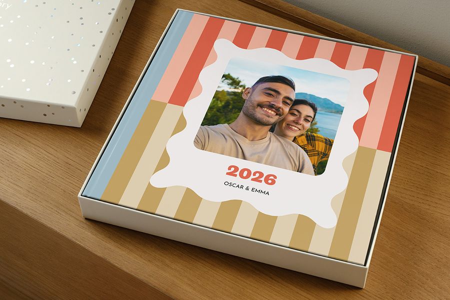 Un livre photo repose dans la boîte cadeau, couvercle retiré, ressemblant à un livre souvenir de l'année intitulé « 2026 » avec un couple souriant sur la couverture, illustrant comment choisir la bonne taille de boîte de présentation pour son livre photo.