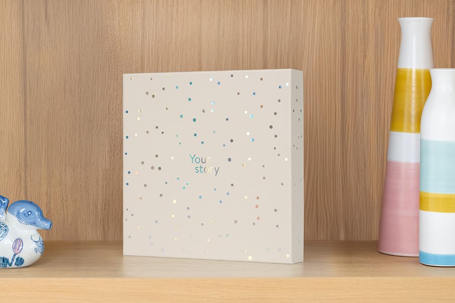 La boîte de présentation est posée sur une étagère à côté d'un vase et de bibelots, illustrant comment elle fait aussi office de jolie boîte de rangement pour album photo.