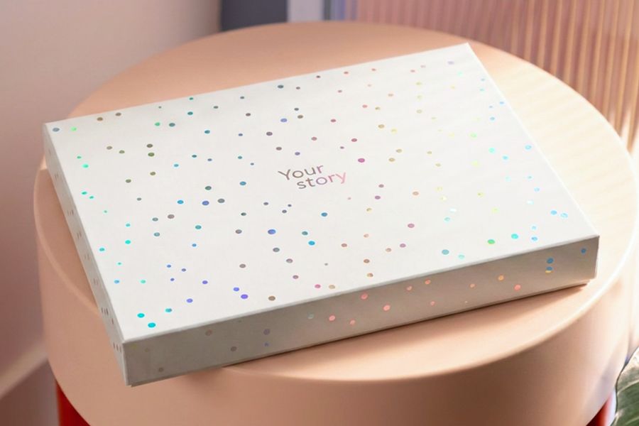 La boîte de présentation fermée est posée sur un tabouret, illustrant l'aspect final de la nouvelle boîte cadeau pour livre photo de Photobox.