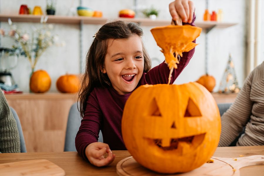 Un enfant soulève le haut d'une citrouille qu'il vient de sculpter, illustrant les citations et phrases drôles et mignonnes sur les citrouilles de Photobox pour les légendes Instagram d'Halloween.