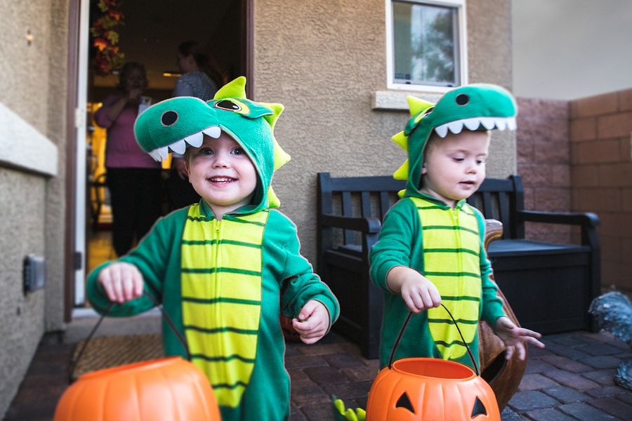 Deux petits garçons déguisés en dinosaures font la chasse aux bonbons en tenant des paniers en forme de citrouille, illustrant les légendes et phrases d'Halloween de Photobox pour les photos de la chasse aux bonbons.