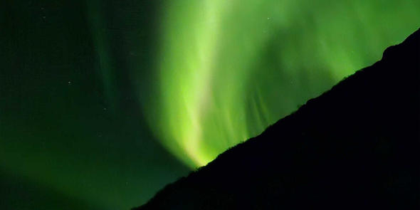 Aurores boréales d’un vert très vif dans le ciel, illustrant les conseils de Photobox pour photographier les aurores boréales.