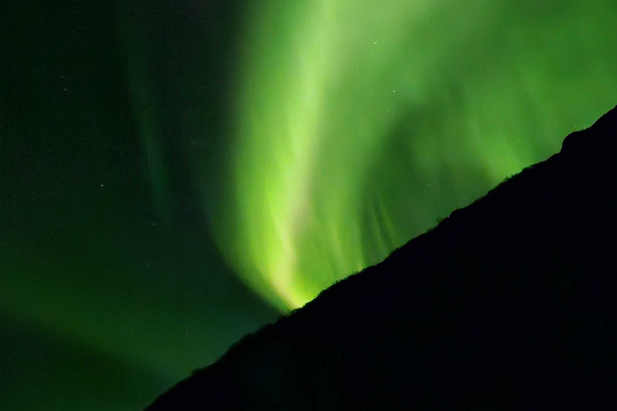 Aurores boréales d’un vert très vif dans le ciel, illustrant les conseils de composition de Photobox pour photographier les aurores boréales.