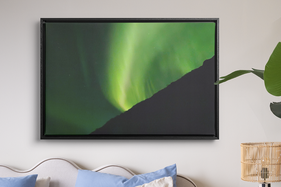 Un tirage encadré d’aurores boréales très vertes accroché au mur au-dessus d’un lit et d’une lampe en raphia, illustrant la décoration murale de Photobox pour transformer vos photos d’aurores boréales en souvenirs à garder.