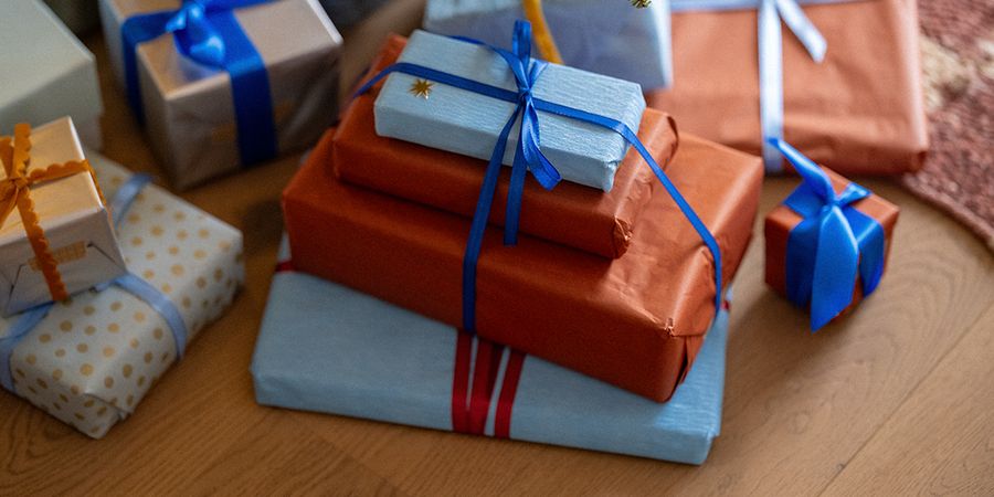 Une pile de cadeaux emballés dans du papier orange et bleu pâle, noués de rubans bleus, illustrant les conseils de Photobox pour les cadeaux de Noël du Black Friday.