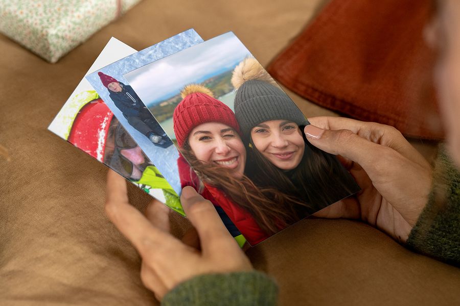 Personne tenant des tirages photo dans les mains, dont celui du dessus montre deux femmes souriantes en bonnets et manteaux d’hiver, pour illustrer les conseils de Photobox pour trouver les bonnes photos d’un cadeau photo personnalisé.