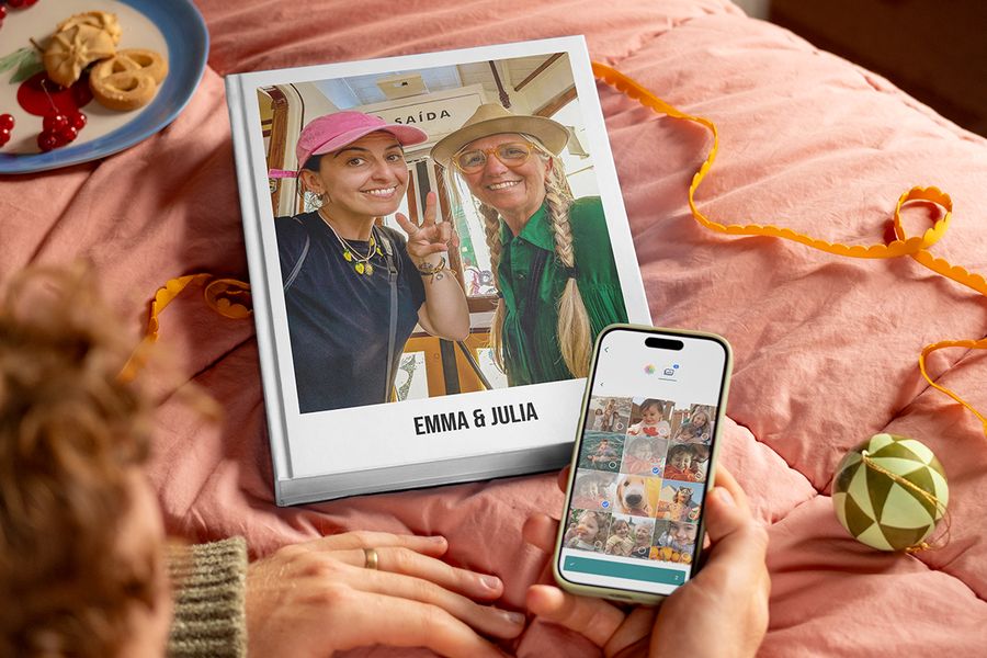 Livre photo personnalisé intitulé « Emma and Julia » avec une mère et sa fille adulte en couverture, à côté des mains d’un homme tenant un téléphone pour montrer combien il est facile de sélectionner des photos et de créer un livre photo Photobox, pour illustrer les conseils de Photobox pour rassembler les photos de ses proches pour un cadeau personnalisé.