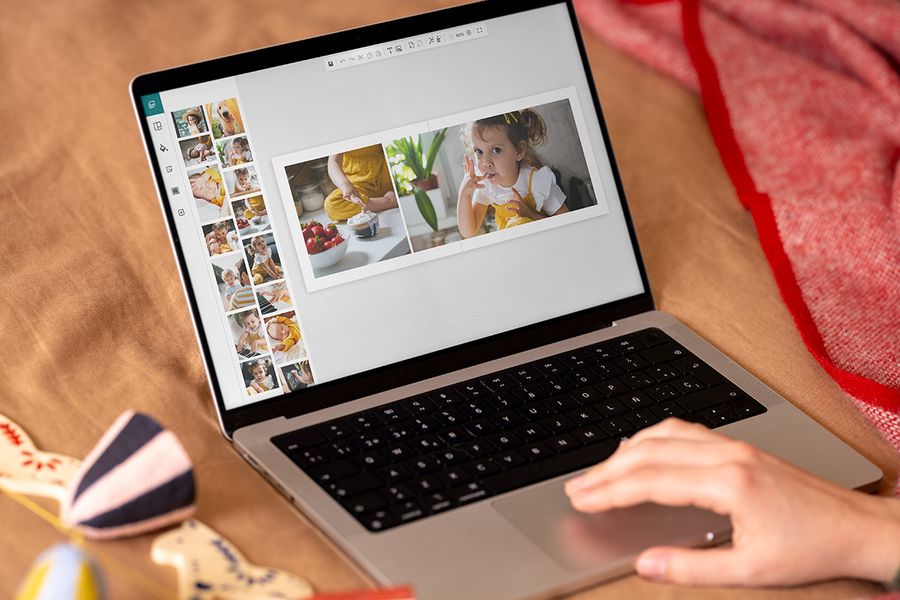 Mains devant un ordinateur portable montrant l’éditeur en ligne de Photobox, pour montrer combien il est facile de créer un livre photo en cadeau de Noël personnalisé, pour illustrer le calendrier de Photobox pour créer un cadeau photo personnalisé.