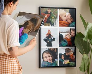 Une femme sourit en tenant une déco photo à côté d'une toile pêle-mêle.