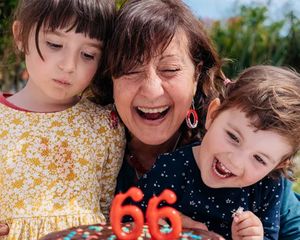 Une grand-mère fête ses 66 ans avec ses deux petits-enfants à ses côtés, prête à souffler les bougies de son gâteau, pour inspirer des idées de cadeaux d’anniversaire dans le guide ultime des cadeaux d’anniversaire Photobox.