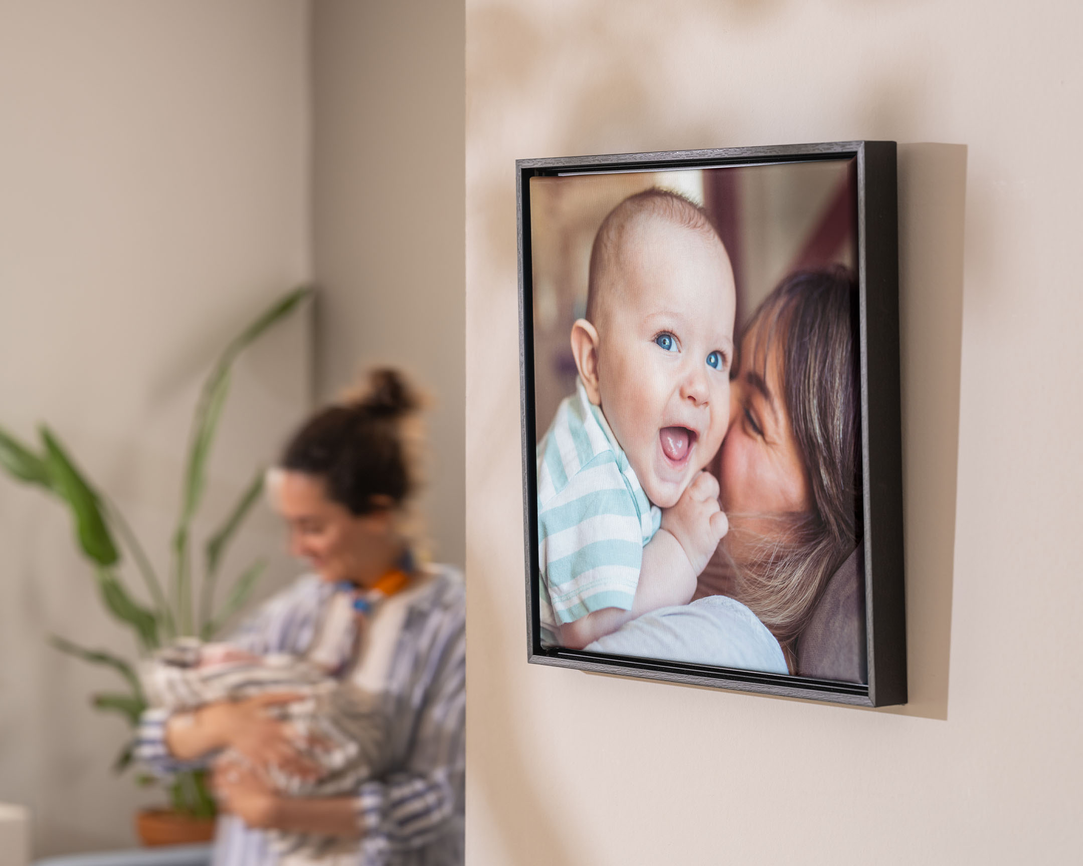 Toile photo encadrée montrant une mère serrant son bébé dans ses bras, accrochée au mur