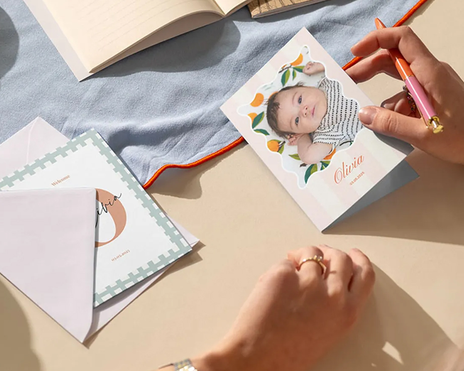 Des mains écrivant une carte personnalisée d'une photo de bébé sur un bureau.