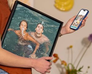 Une femme tient une décoration murale Photobox montrant une famille jouant dans l’eau pendant les vacances, une belle idée pour transformer des photos de vacances en déco murale.